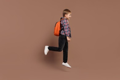 Happy schoolboy with backpack jumping on brown background