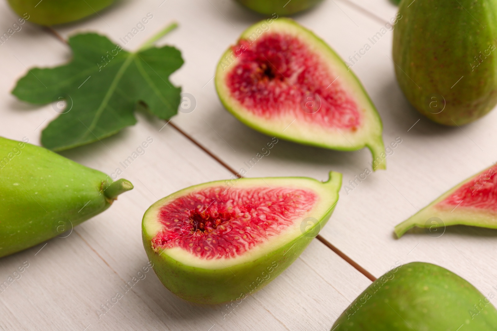 Photo of Cut and whole green figs on white wooden table, closeup