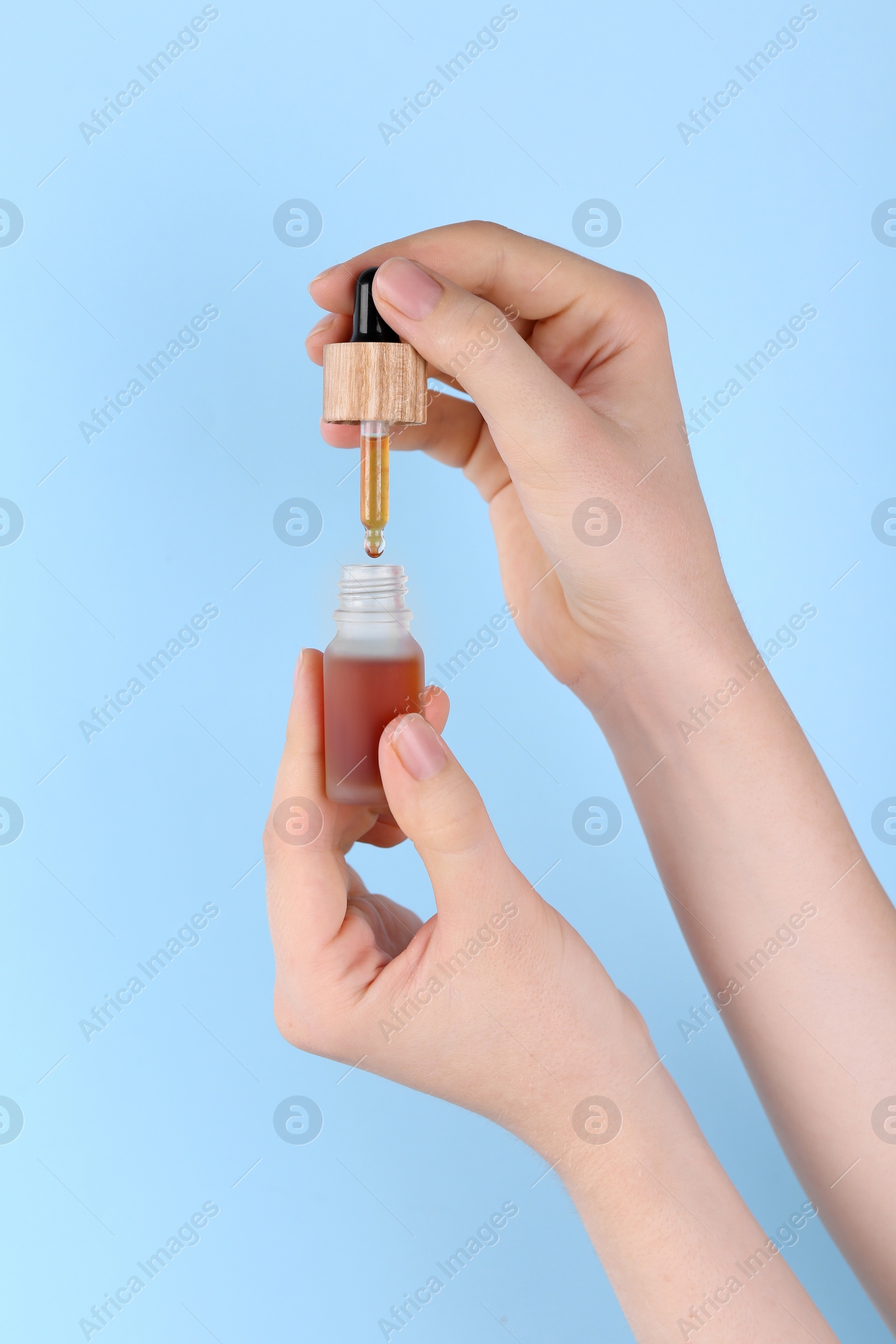 Photo of Woman holding bottle of essential oil on light blue background, closeup