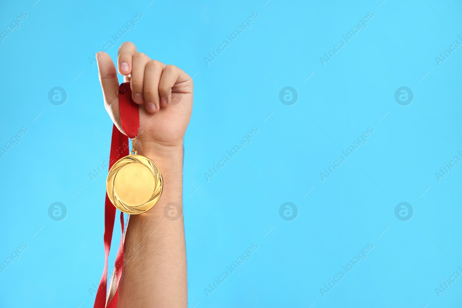 Photo of Man holding golden medal on light blue background, closeup. Space for design