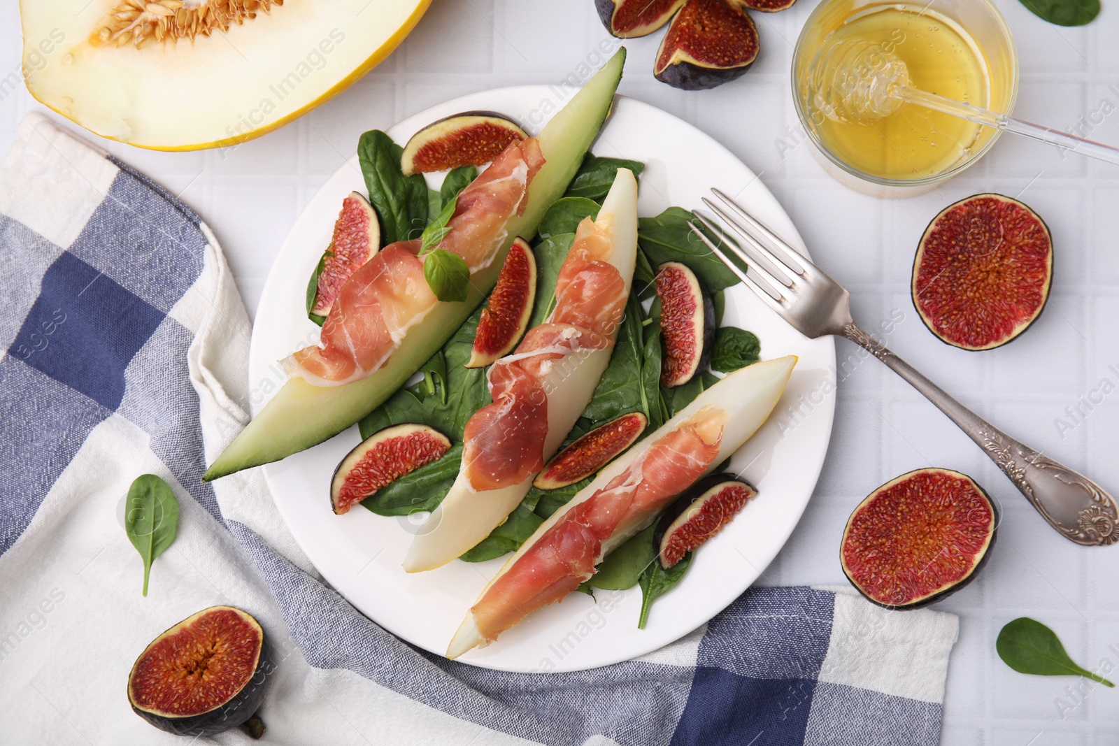 Photo of Tasty melon, jamon and figs served on white tiled table, flat lay