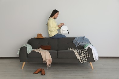 Photo of Young woman holding backpack on sofa with clothes indoors