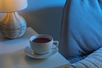 Cup of hot tea and nightlight on white table at night