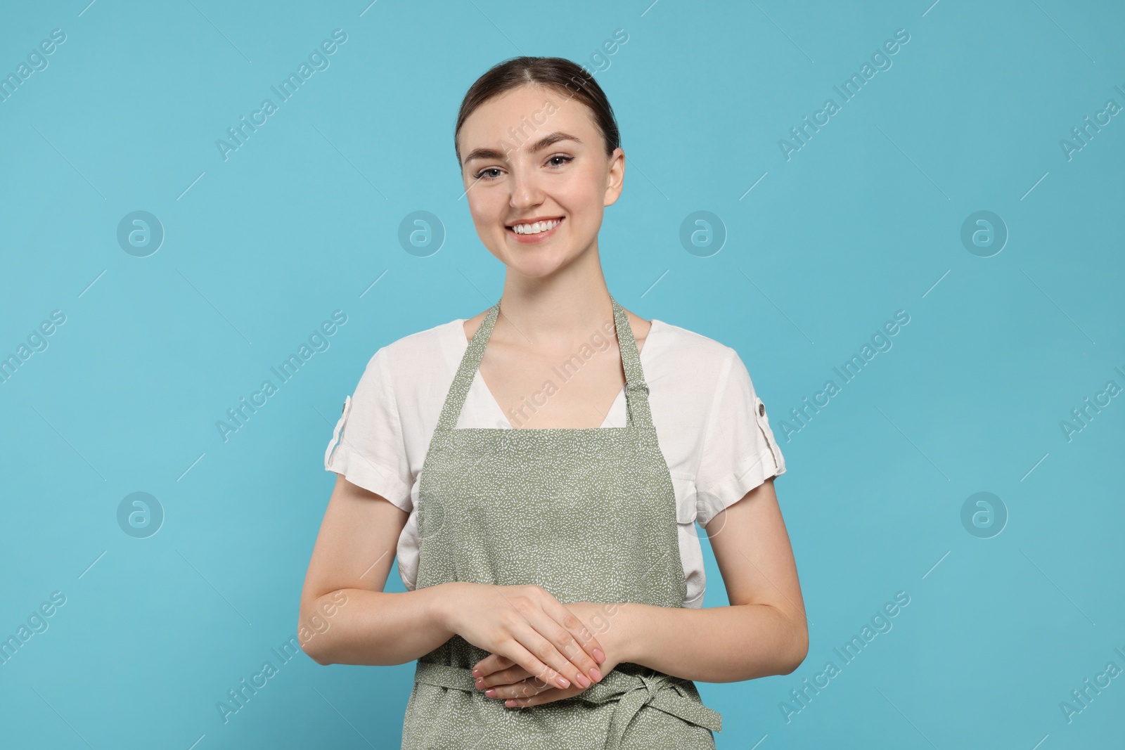 Photo of Beautiful young woman in clean apron with pattern on light blue background