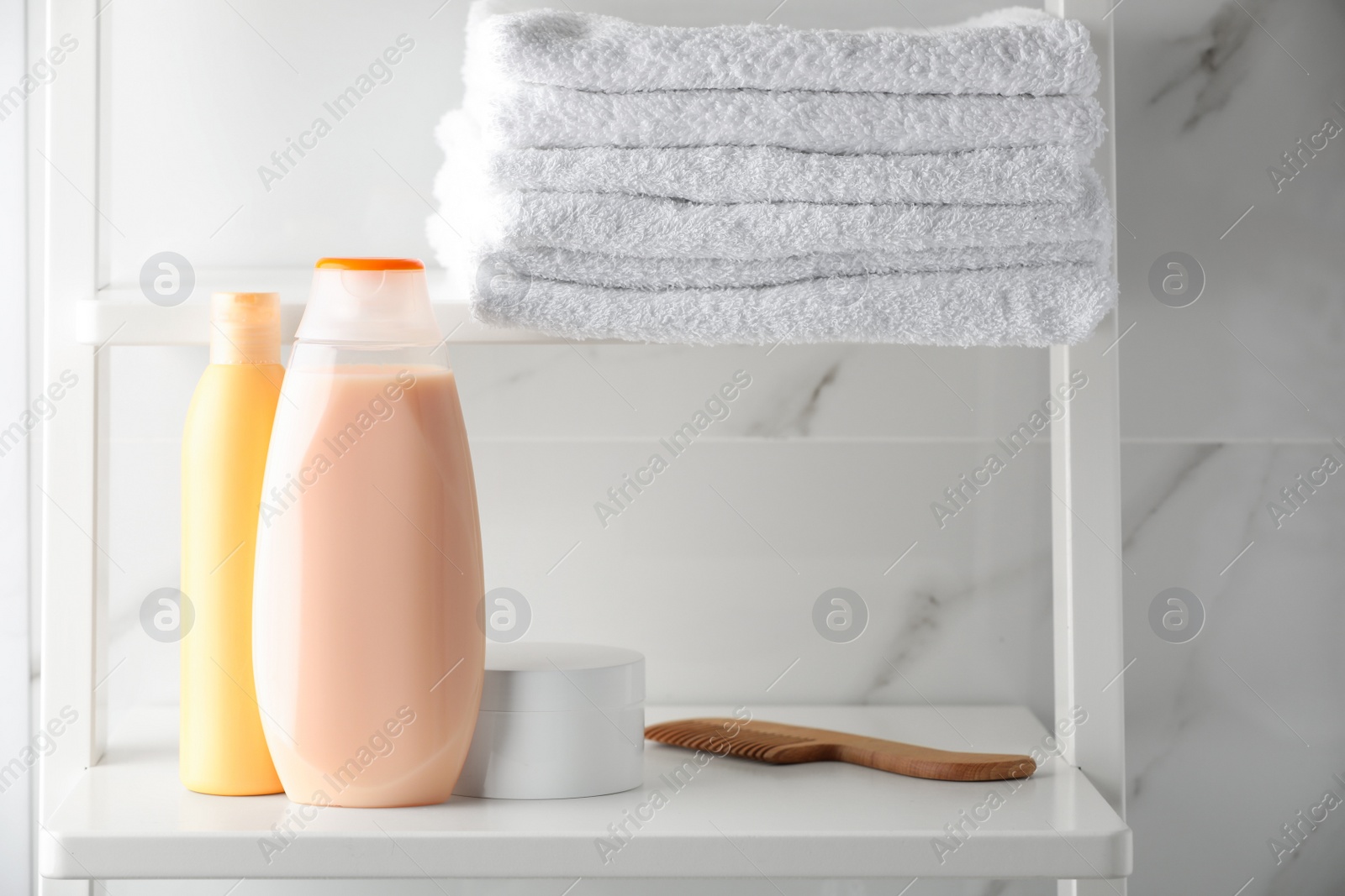 Photo of Stack of towels, comb, shampoo and other toiletries on shelves near white marble wall