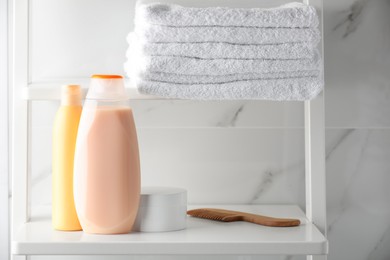 Stack of towels, comb, shampoo and other toiletries on shelves near white marble wall