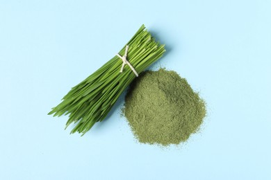 Photo of Pile of wheat grass powder and fresh sprouts on light blue table, flat lay