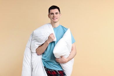 Happy man in pyjama holding pillow and blanket on beige background