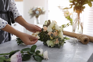 Photo of Florist tieing bow of beautiful wedding bouquet at light grey marble table, closeup
