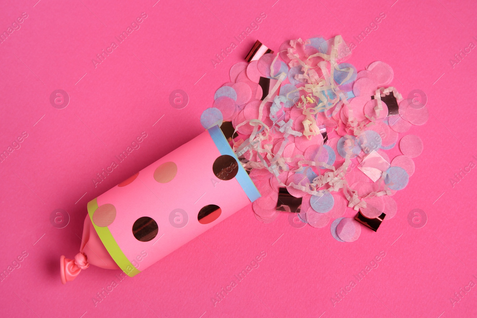 Photo of Beautiful serpentine and confetti bursting out of party popper on pink background, flat lay