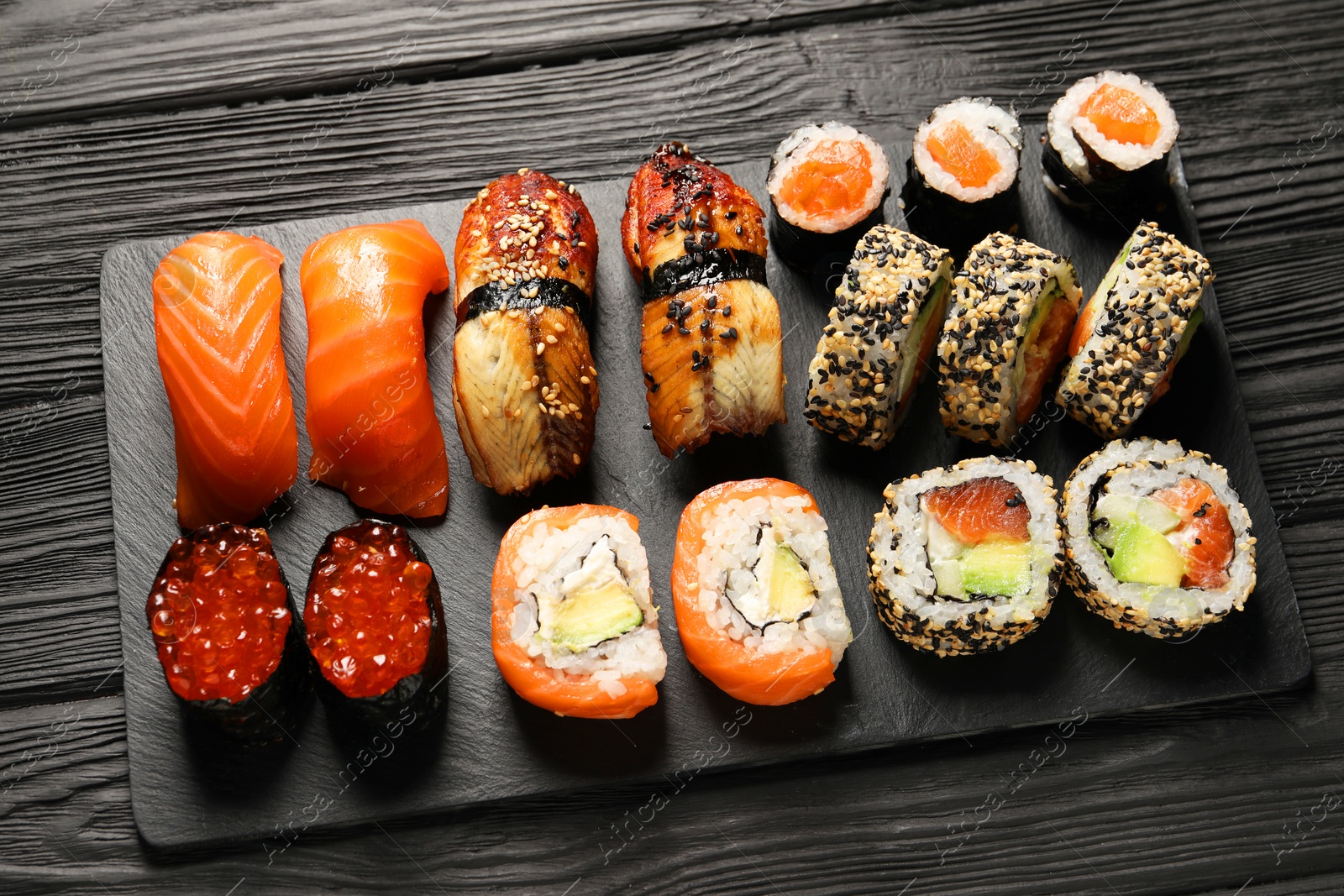 Photo of Set of delicious sushi rolls on black wooden table, above view