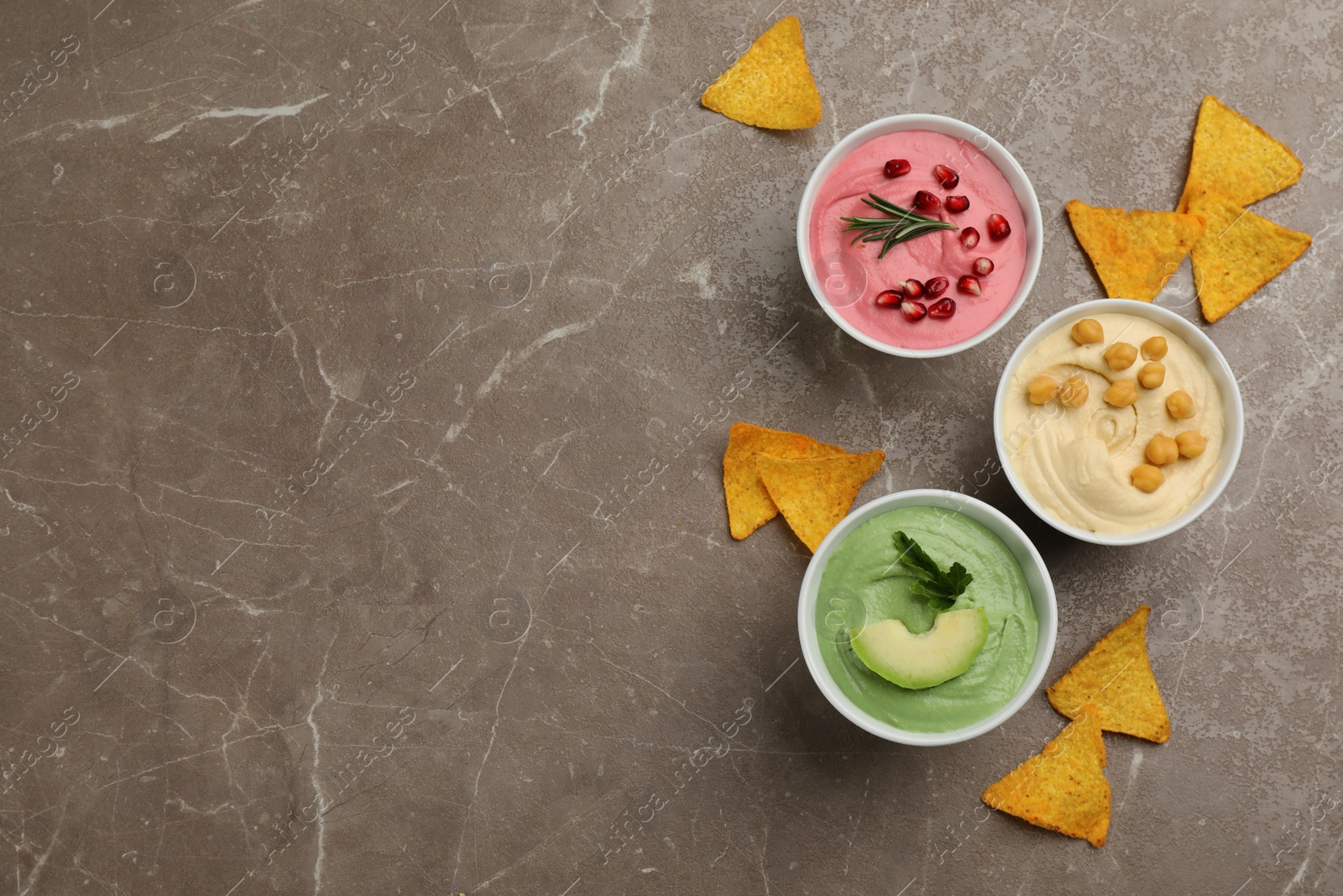 Photo of Different delicious hummuses with tortilla chips on brown marble table, flat lay. Space for text