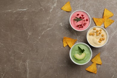 Photo of Different delicious hummuses with tortilla chips on brown marble table, flat lay. Space for text