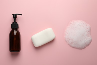 Photo of Dispenser and soap bar with fluffy foam on pink background, flat lay