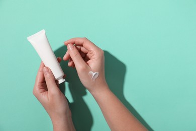 Woman with tube of hand cream on turquoise background, top view. Space for text