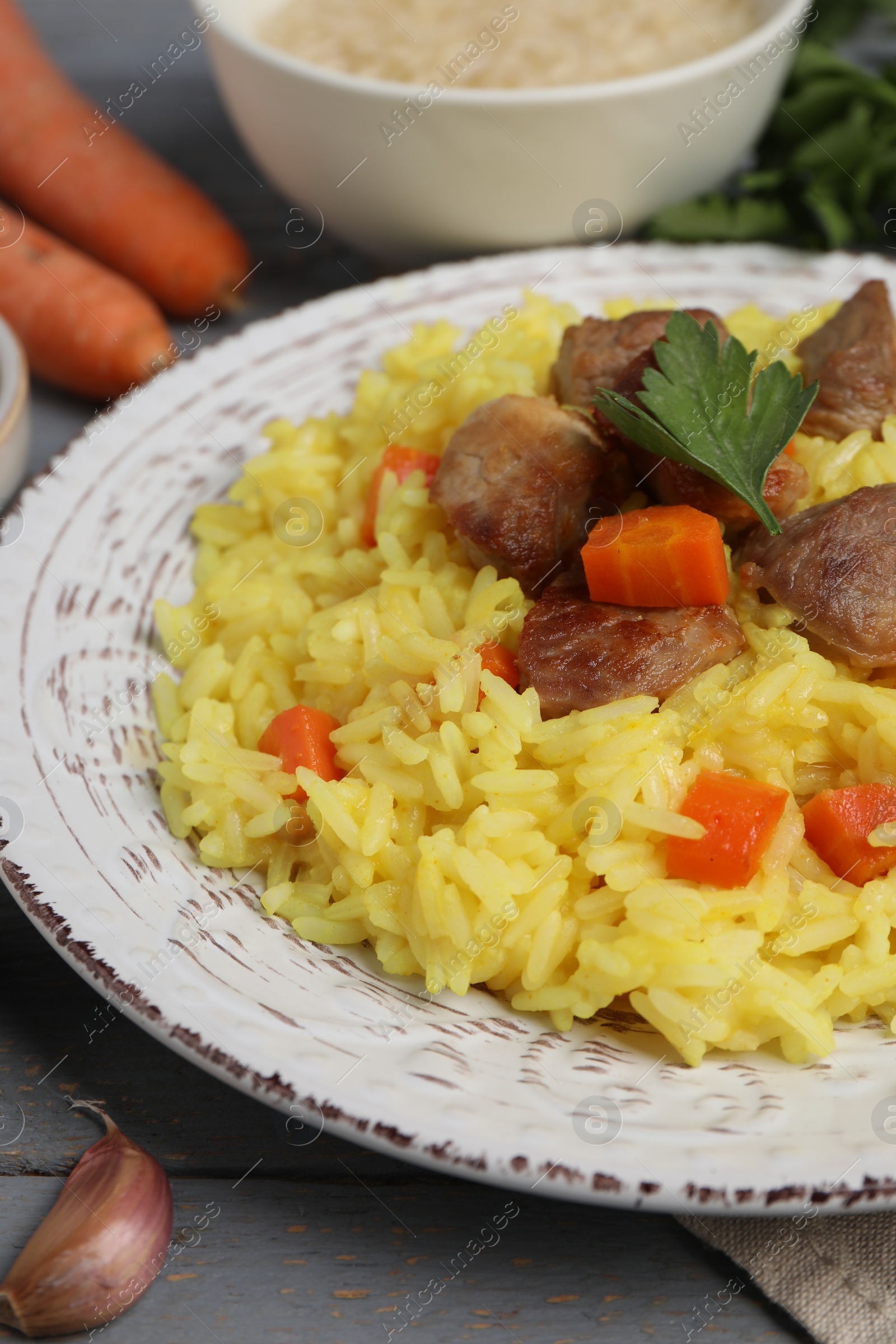 Photo of Delicious pilaf with meat and carrot on grey wooden table, closeup