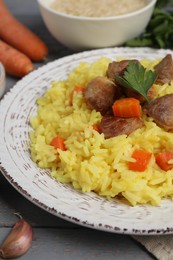 Delicious pilaf with meat and carrot on grey wooden table, closeup