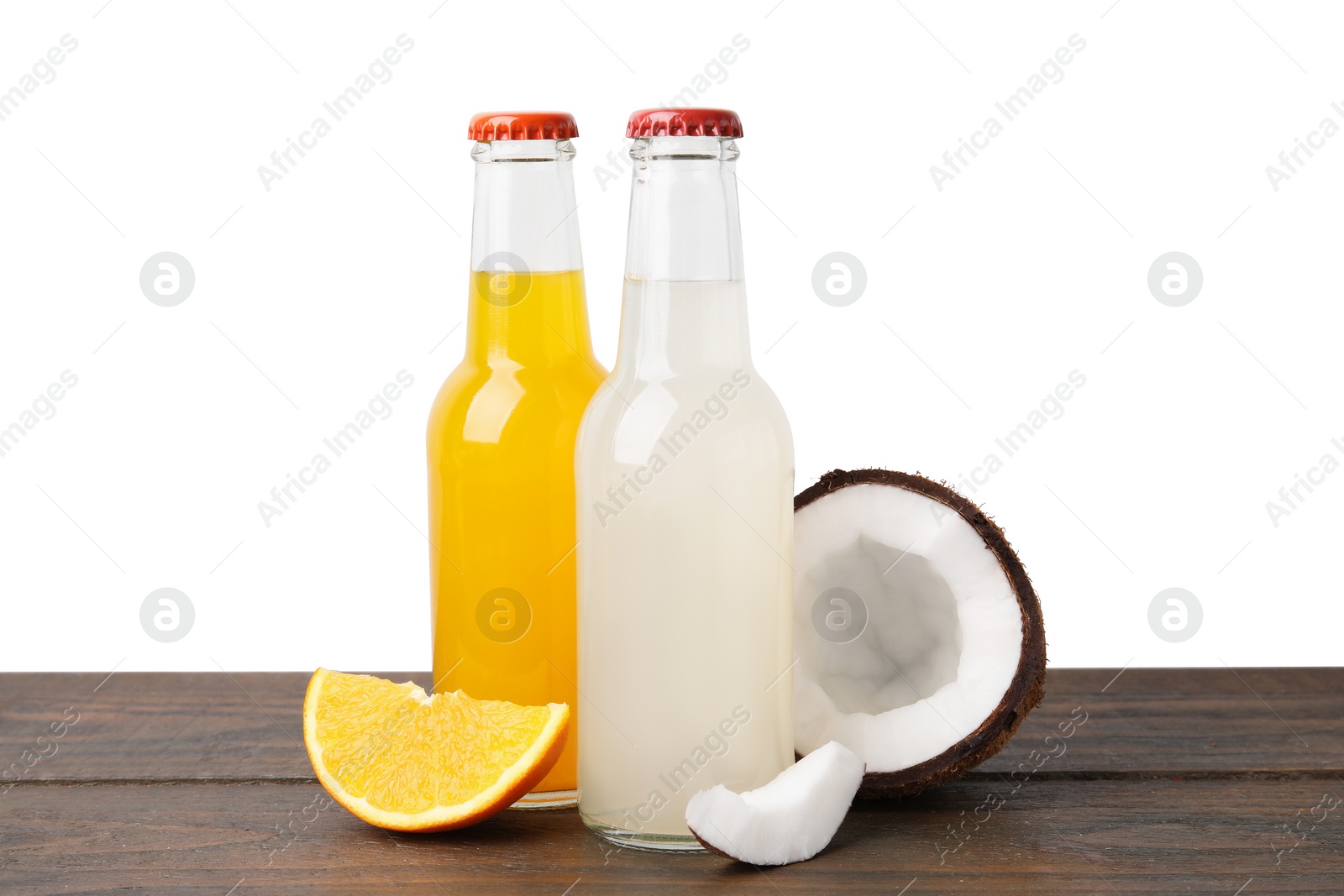 Photo of Delicious kombucha in glass bottles, orange and coconut on wooden table against white background