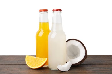 Photo of Delicious kombucha in glass bottles, orange and coconut on wooden table against white background