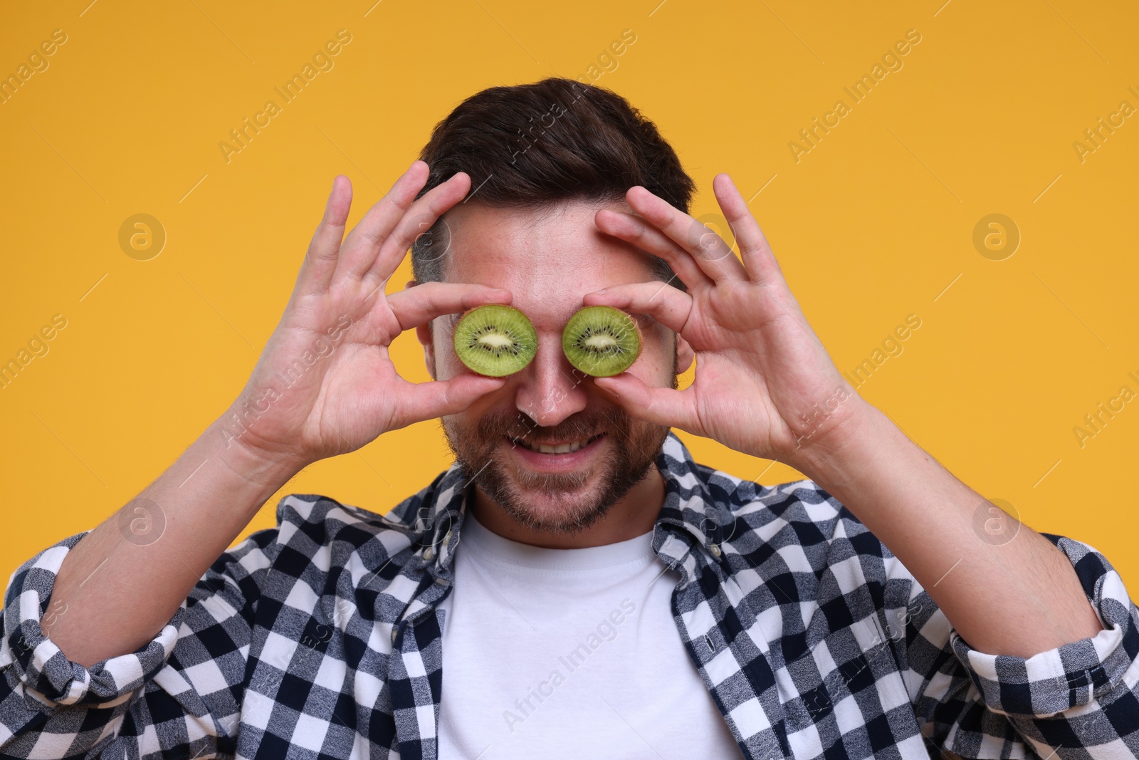 Photo of Man covering his eyes with halves of kiwi on yellow background