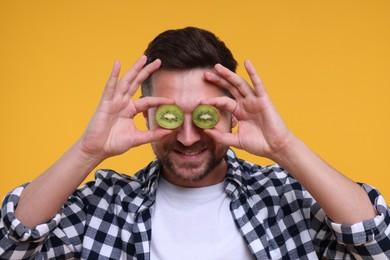 Photo of Man covering his eyes with halves of kiwi on yellow background