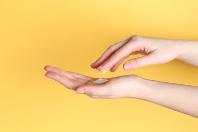 Photo of Woman applying cream on her hand against yellow background, closeup