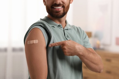 Photo of Man pointing at sticking plaster after vaccination on his arm at home, closeup