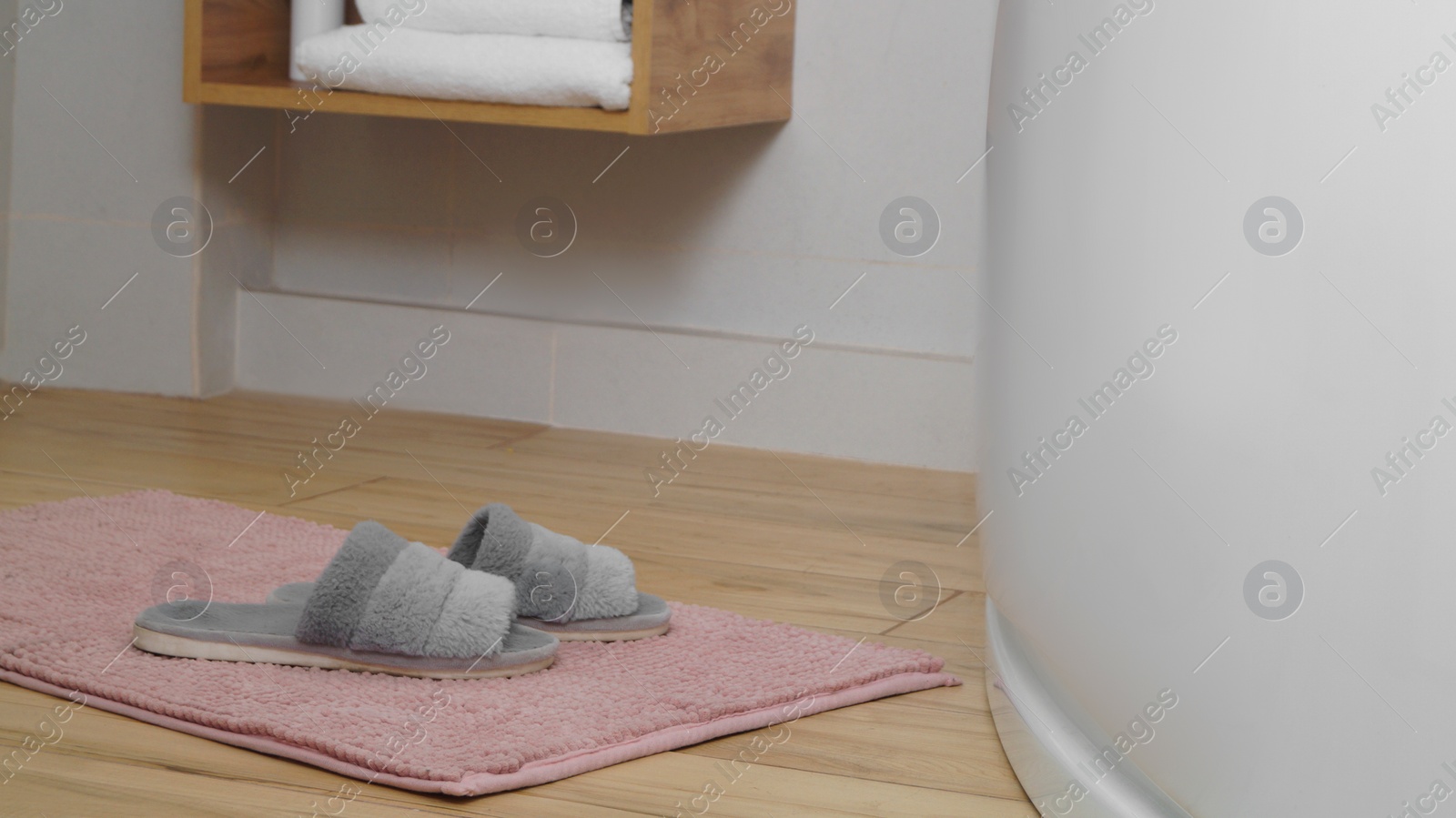 Photo of Mat with soft slippers near tub on wooden floor in bathroom