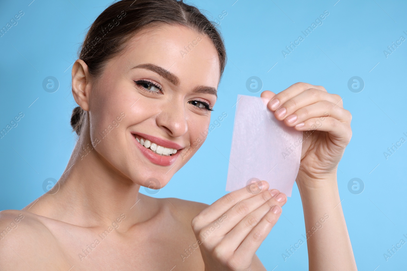 Photo of Beautiful woman with mattifying wipe on light blue background