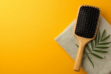 Wooden hairbrush, towel and green leaves on orange background, top view. Space for text