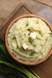 Photo of Bowl of delicious mashed potato with dill and butter on wooden table, flat lay