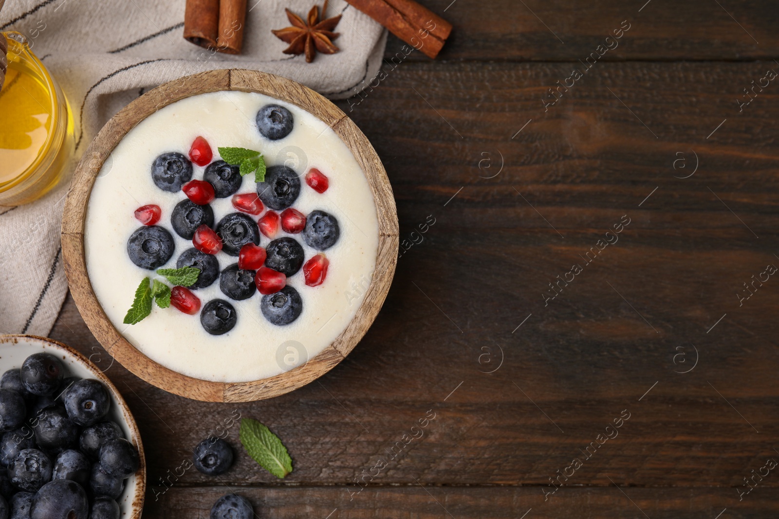 Photo of Bowl of delicious semolina pudding with blueberries, pomegranate and ingredients on wooden table, flat lay. Space for text