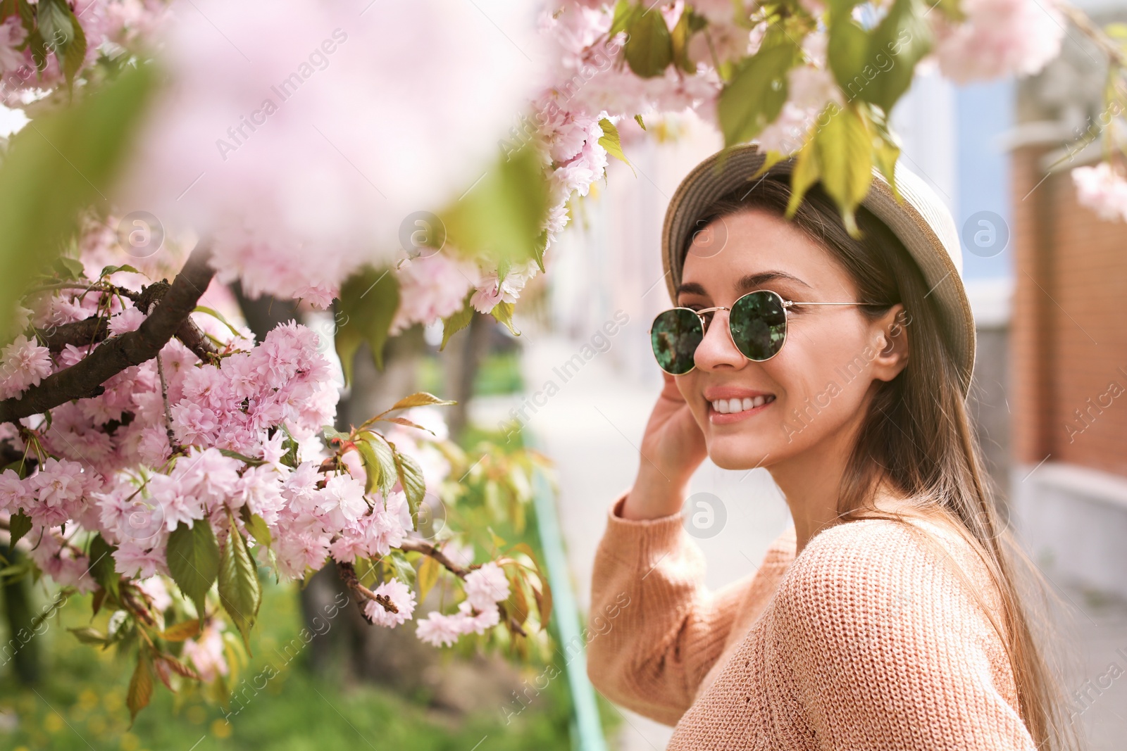 Photo of Happy stylish young woman near blossoming sakura tree outdoors. Spring look