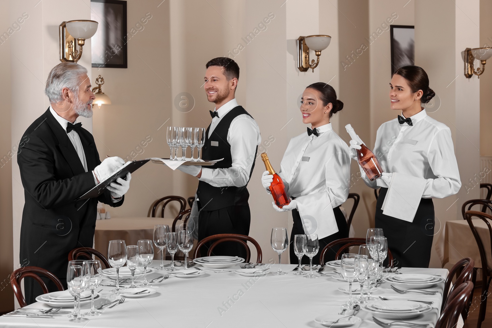 Photo of Senior man wearing formal suit teaching trainees in restaurant. Professional butler courses