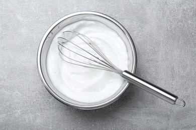 Photo of Whipped egg whites with balloon whisk on grey table, top view