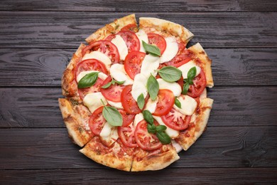 Photo of Delicious Caprese pizza with tomatoes, mozzarella and basil on dark wooden table, top view