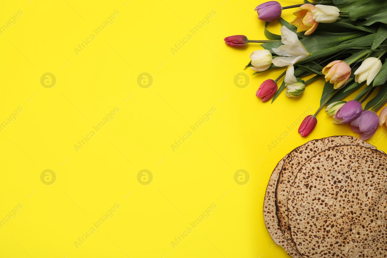 Photo of Tasty matzos and fresh flowers on yellow background, flat lay with space for text. Passover (Pesach) celebration