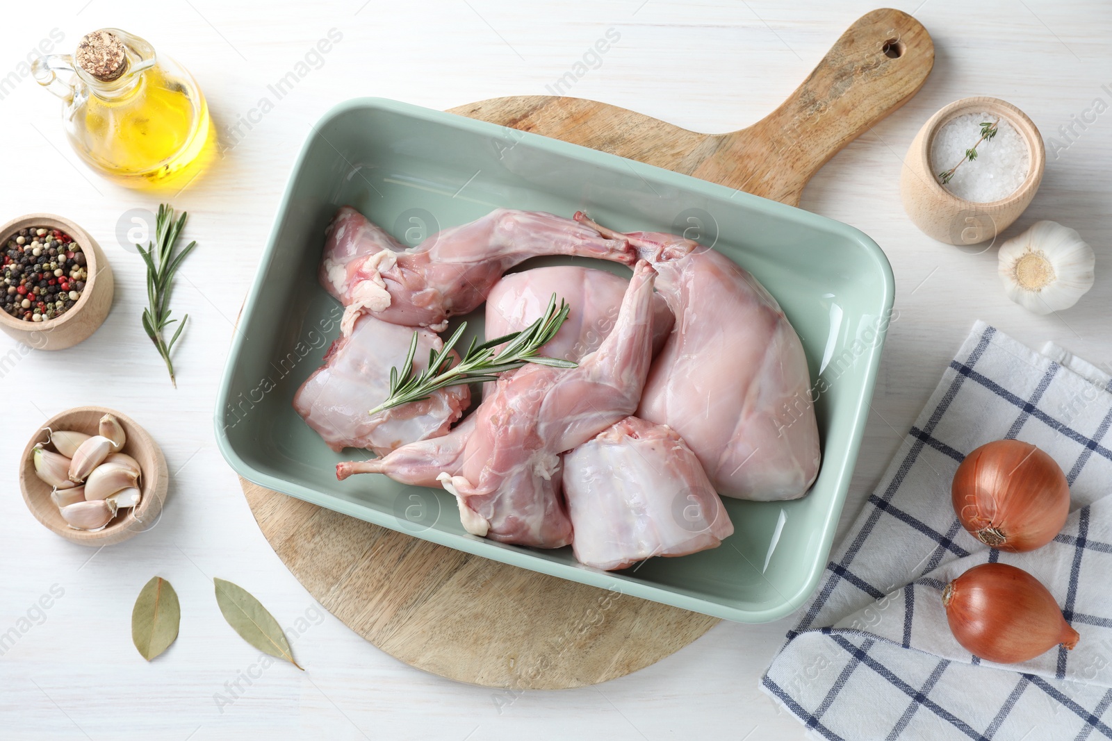 Photo of Raw rabbit meat in baking dish and products on white wooden table, flat lay