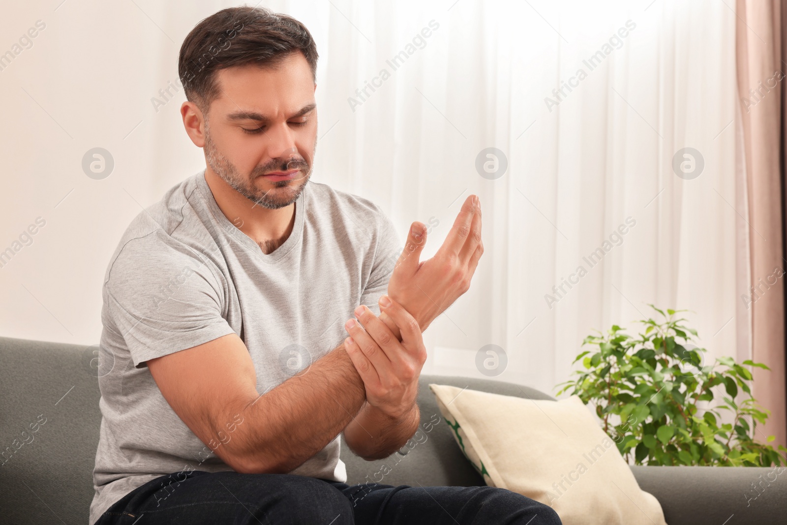 Photo of Man suffering from pain in his hand on sofa indoors