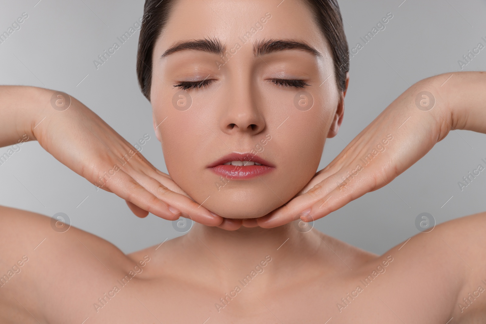 Photo of Young woman massaging her face on grey background