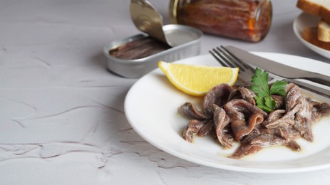 Photo of Plate with canned anchovy fillets and lemon wedge on white textured table, closeup. Space for text