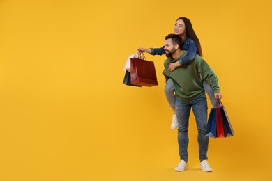 Photo of Happy couple with shopping bags on orange background. Space for text