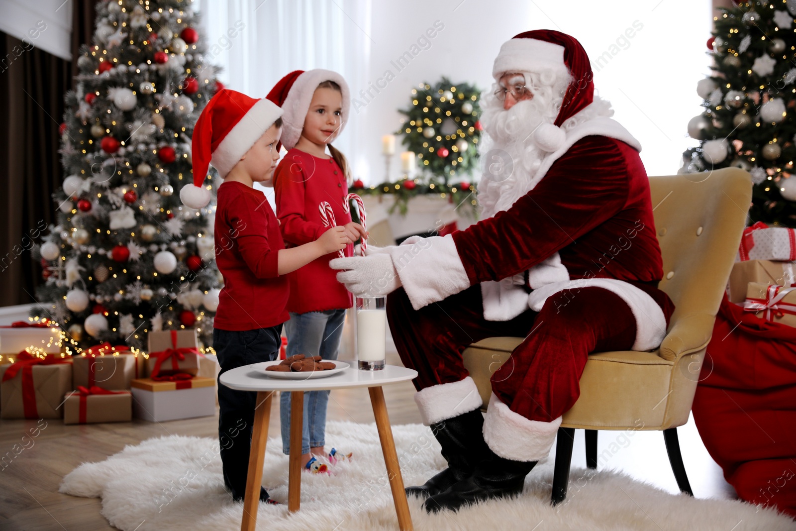 Photo of Santa Claus giving candy canes to children in room decorated for Christmas