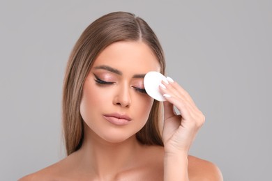 Photo of Beautiful woman removing makeup with cotton pad on grey background