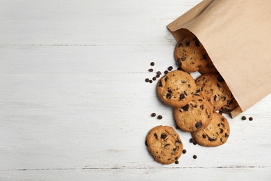 Photo of Paper bag with delicious chocolate chip cookies on wooden table, flat lay. Space for text