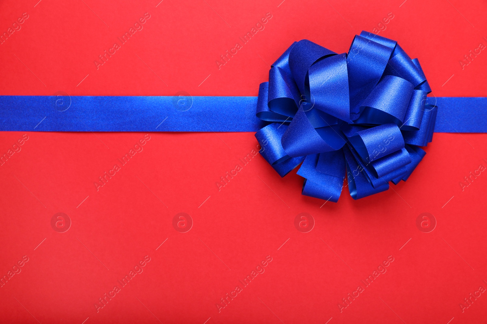 Photo of Blue ribbon with bow on red background, top view. Space for text