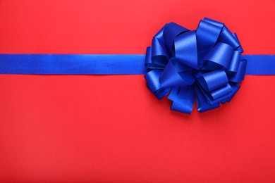 Photo of Blue ribbon with bow on red background, top view. Space for text