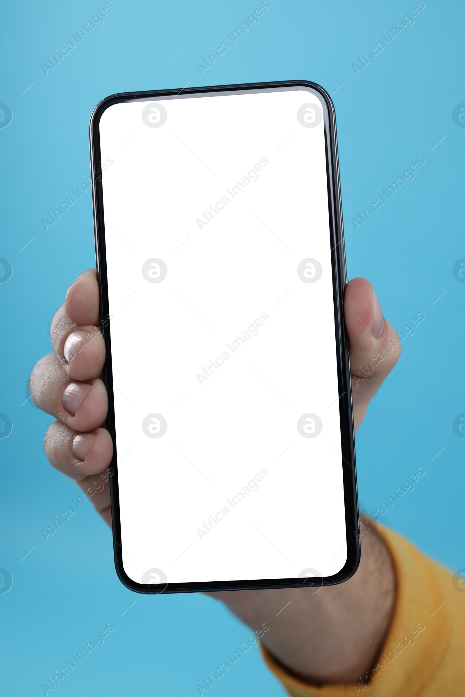 Photo of Man holding smartphone with blank screen on light blue background, closeup