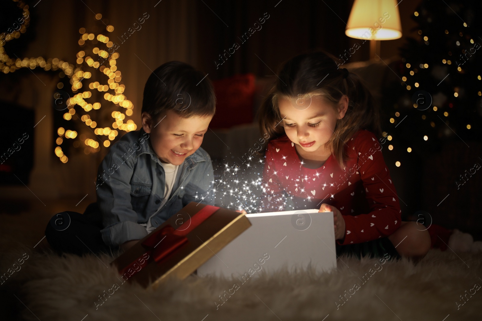 Photo of Cute children opening gift box in room decorated for Christmas