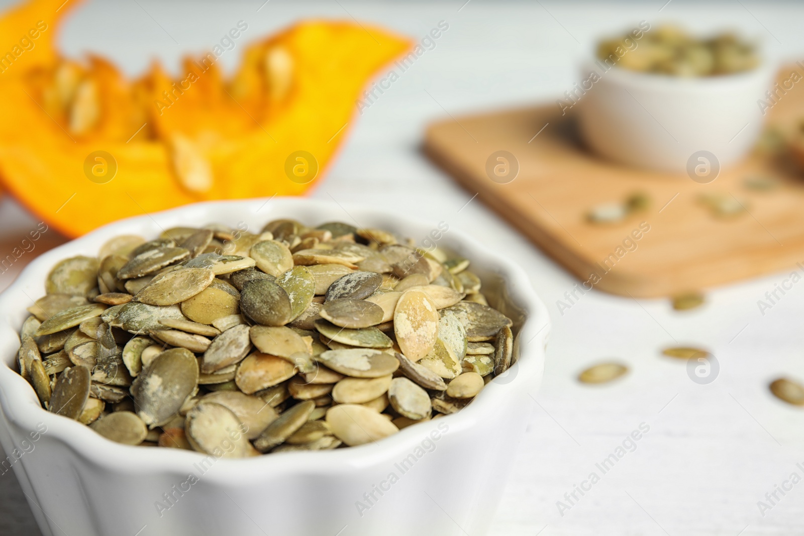 Photo of Bowl of raw pumpkin seeds on white table, closeup. Space for text